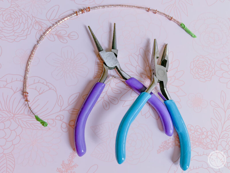Two pairs of jewelry pliers and a section of rose gold seed beads