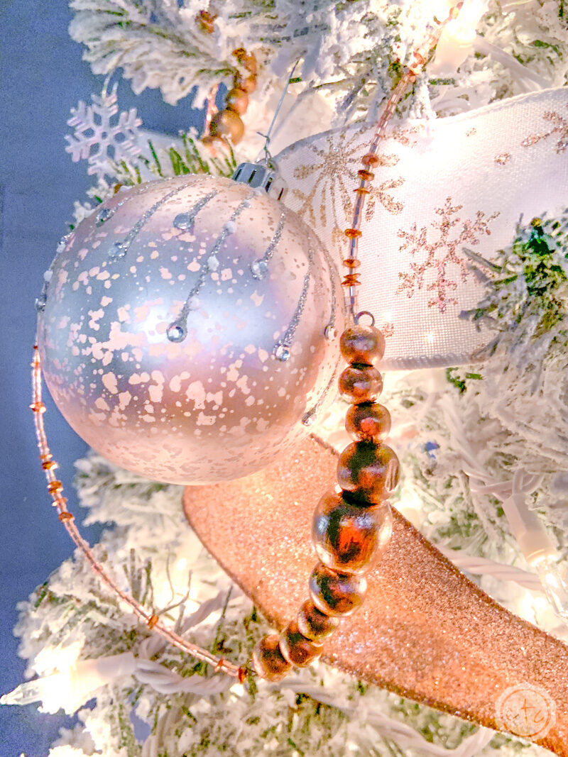 A rose gold mercury glass ornament next to a rose gold wood bead garland